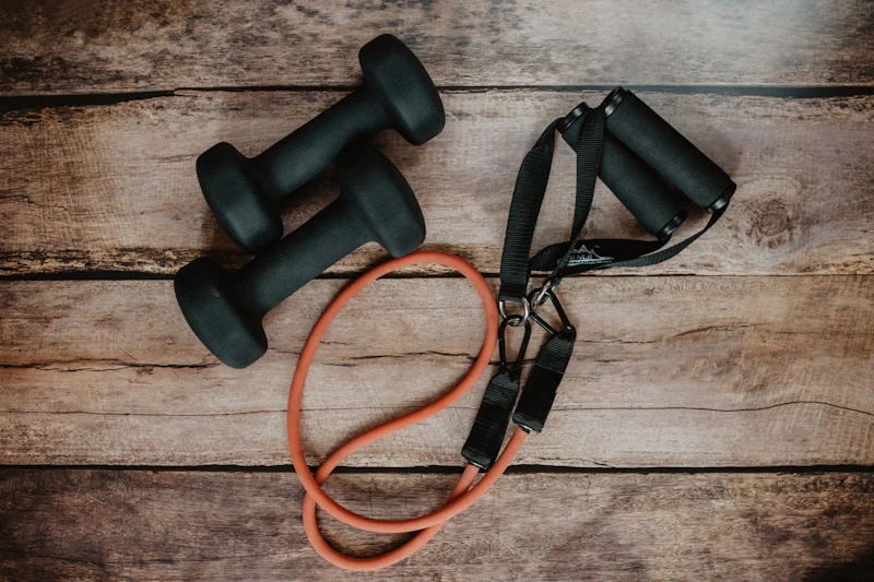 Two dumbbells and an orange resistance band on a wooden floor